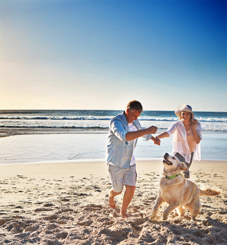 Pareja jugando con su perro en la playa