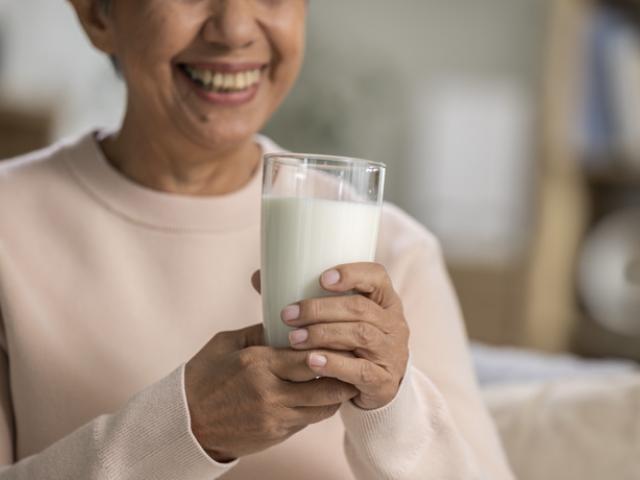 Mujer adulta mayor disfrutando un vaso de leche, fuente de calcio clave para prevenir la osteoporosis.